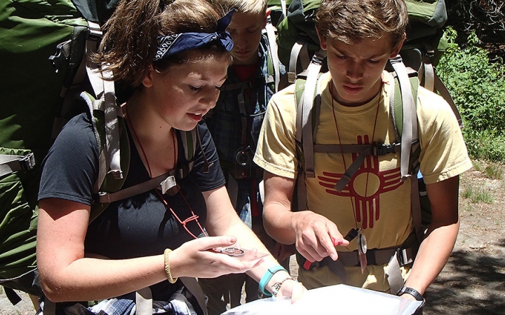 Two people wearing backpacks examine a map.